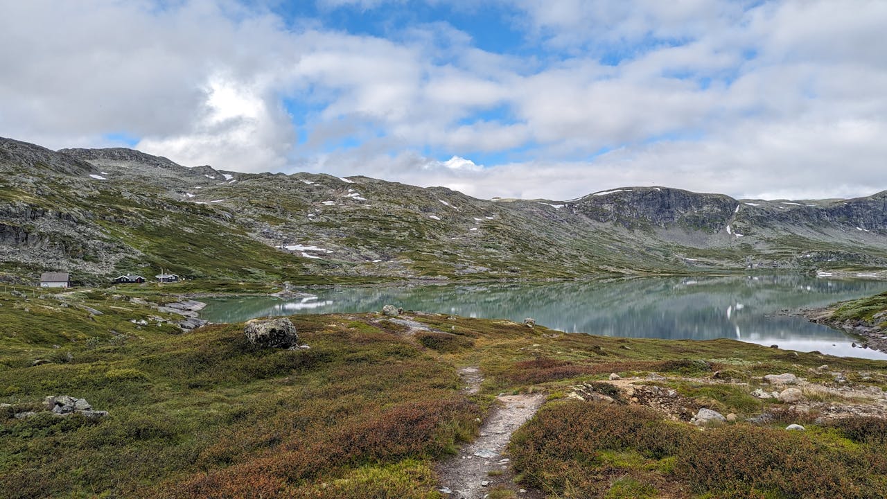 Cyclists on a gravel track across a high Norwegian plateau with patches of snow and mountain ridges — Rallarvegen between Finse and Myrdal.