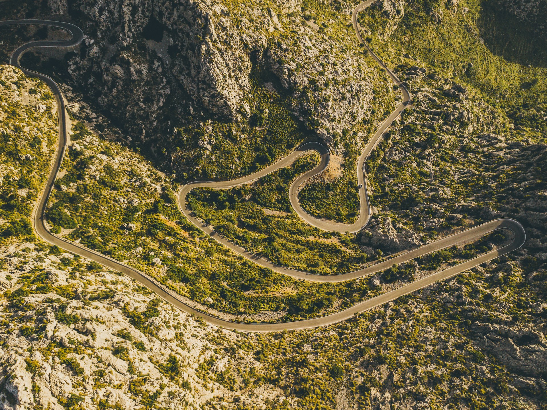 Cyclists climbing the winding hairpins of Sa Calobra, Mallorca — the iconic Coll dels Reis ascent with steep limestone walls and tight switchbacks